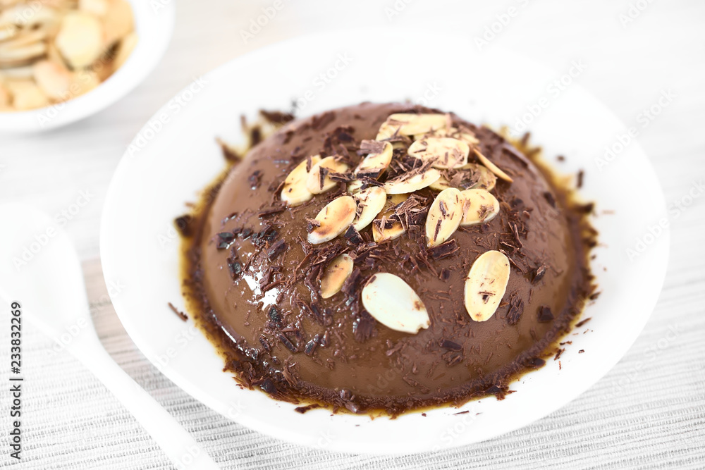 Schokoladenflan mit Karamellsauce, Mandeln und geraspelte Schokolade, fotografiert mit natürlichem Licht (Selektiver Fokus, Fokus in die Mitte des Desserts)