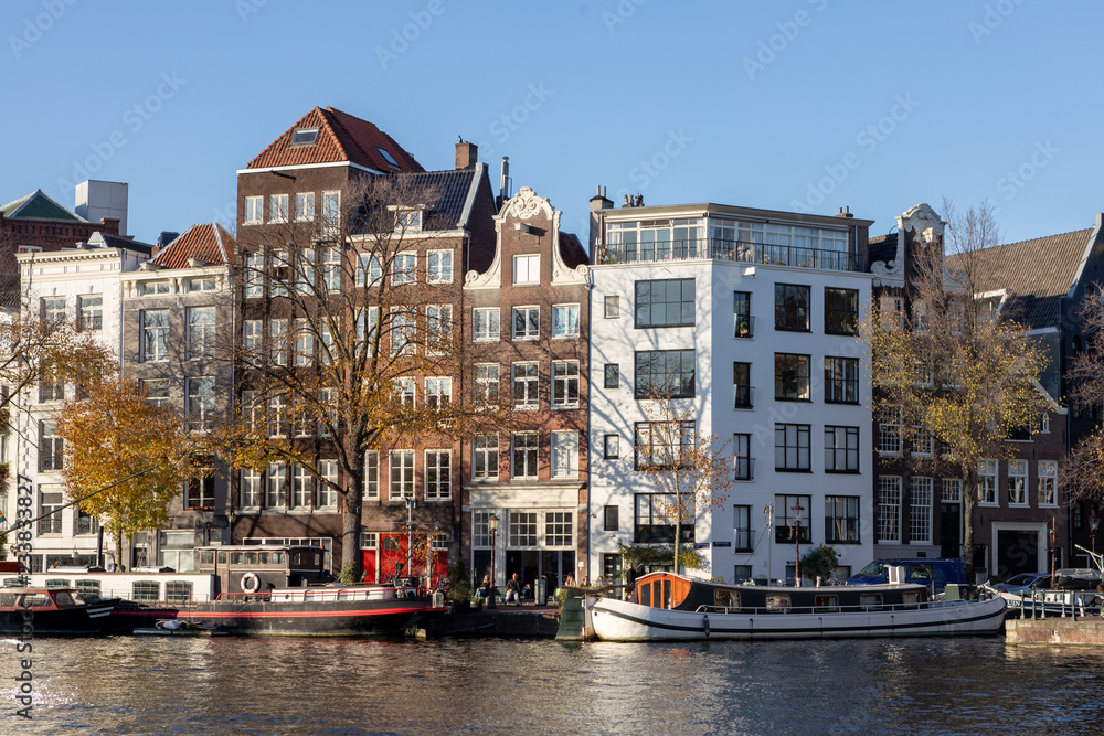 Typical Amsterdam canal houses with residential boats in front and a tourist ship passing by on a sunny day in late afternoon