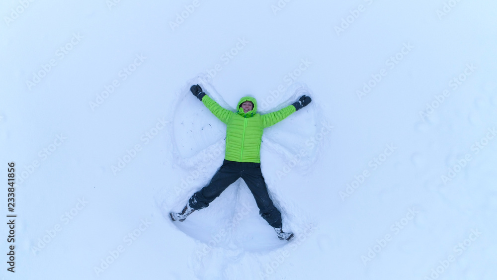 AERIAL Cheerful smiling girl making snow angles in fresh snow on snowy mountain