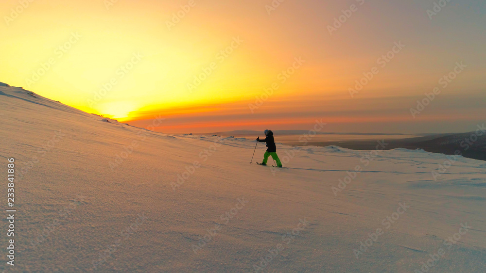 AERIAL: Active woman exploring snowy Lapland wilderness on snowshoes at sunrise