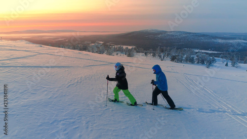 AERIAL Active couple snowshoeing up a mountain slope in snowy Lapland at sunrise