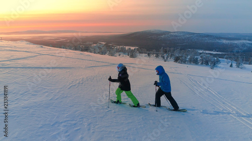 Photography AERIAL Active couple snowshoeing up a mountain slope in snowy Lapland at sunrise