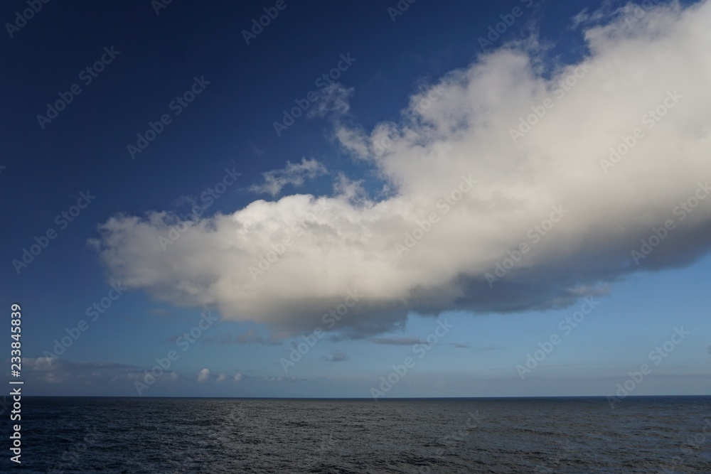 Thick white clouds over the horizon in a deep blue sky somewhere in the North Pacific Ocean between Sitka, Alaska, and Victoria, British Columbia, Canada.