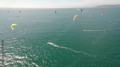 Aerial views across ocean horizon. Multiple colourful para sails blowing in the breeze.