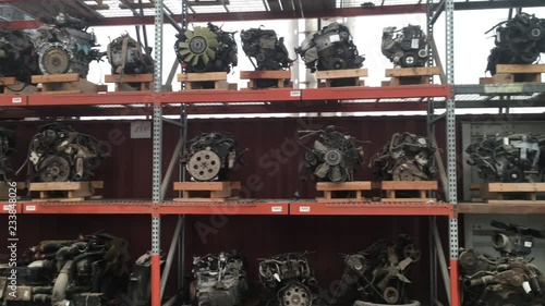 Used car engines and small motors for sale on steel shelves pan from left to right under natural light.