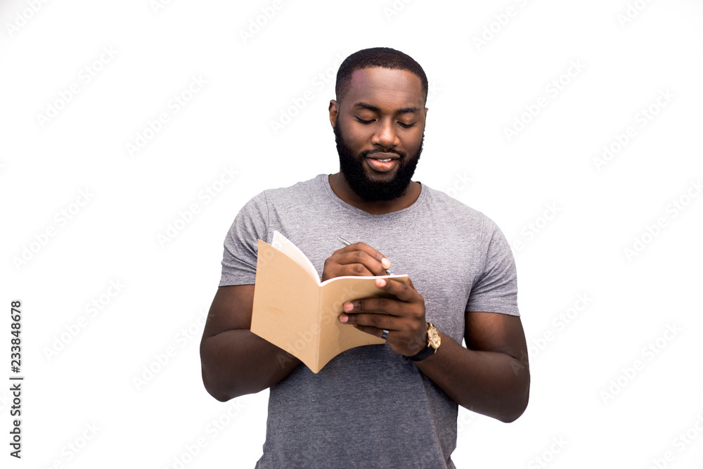 A young handsome African American man writes his plans for the week on a daily planner, is engaged in planning and time management. Responsibility, mobility, the way to success. Isolated A young handsome African American man writes his plans for the week on a daily planner, is engaged in planning and time management. Responsibility, mobility, the way to success. Isolated