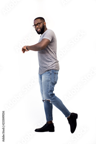 Full-length, successful African American male man strides forward isolated on a white background, looks at the clock on his hand and checks the time, smiles contented, successful and self-confident