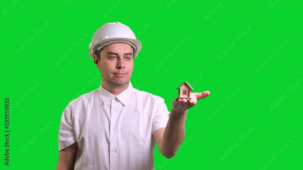 Young male engineer standing and showing hand palm with small model of house on green screen background Young male engineer standing and showing hand palm with small model of house on green screen background