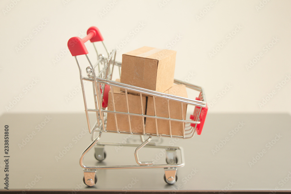 Miniature shopping cart with parcel or paper cartons in trolley on laptop,E-commerce concept. Miniature shopping cart with parcel or paper cartons in trolley on laptop,E-commerce concept.