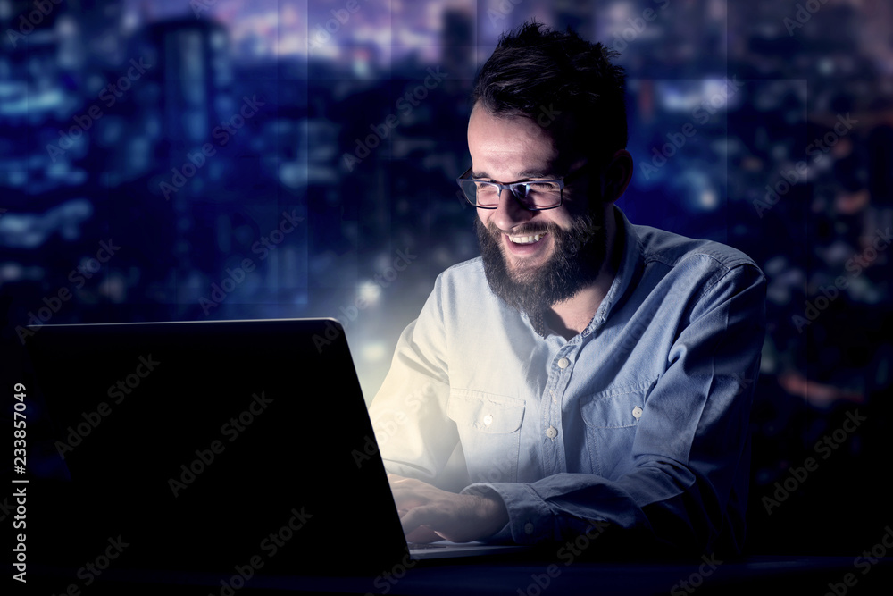 Young handsome businessman working late at night in the office with blue lights in the background