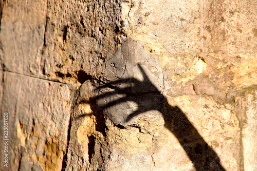 Strange shadow of one hand on an old stone wall. Black shadow, female hand. Background, texture, cropped shot, vertical, abstraction. Concept of fears.