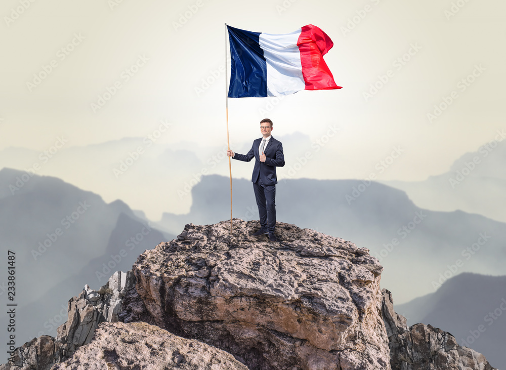 Obraz premium Successful businessman on the top of a mountain holding France victory flag 