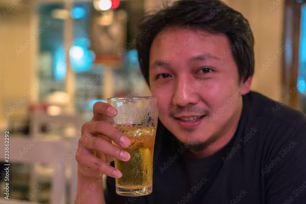 Asian young man in happiness action and drinking beer in pub and restaurant with low light place, relax and drink concept
