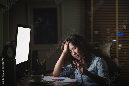 Portrait of Asian Businesswoman sitting and working hard on the table with front of computer desktop in workplace at late with serious action, Work hard and too late concept