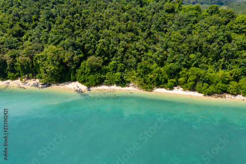 Aerial drone view of an empty tropical sandy beacj surrounded by lush green forest photo