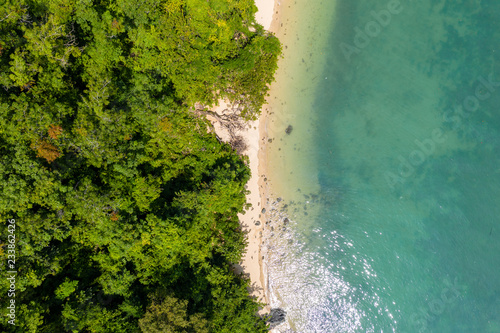 Aerial drone view of an empty tropical sandy beacj surrounded by lush green forest