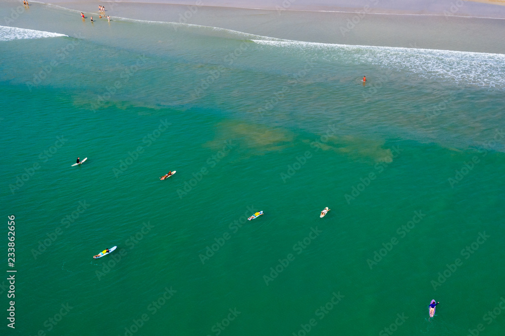 Aerial drone view of surfers waiting for waves in a shallow, tropical ocean