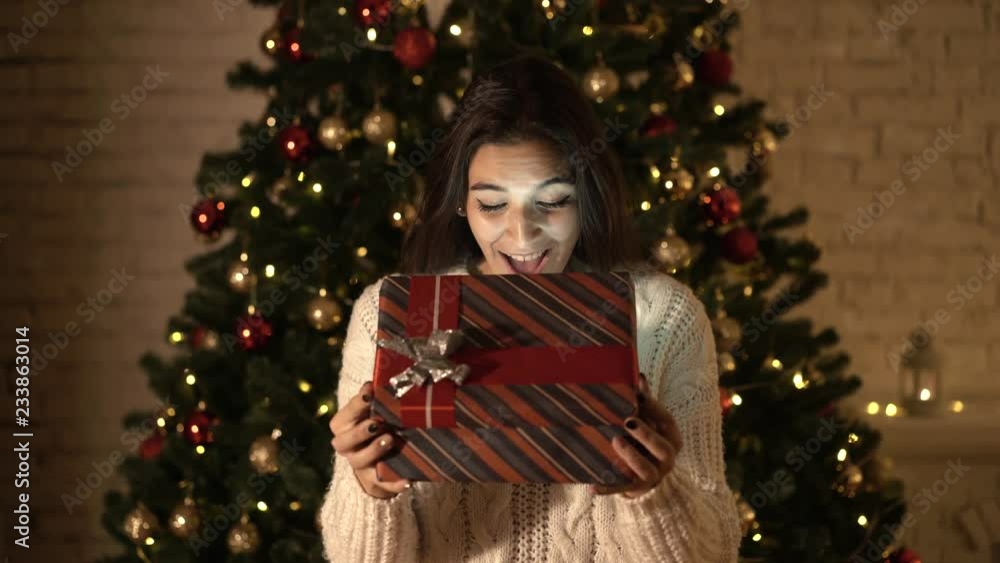 The girl makes a wish and opens a Christmas gift package. the concept of holidays and New year. the girl is happy and smiling with a Christmas gift in her hands. The girl makes a wish and opens a Christmas gift package. the concept of holidays and New year. the girl is happy and smiling with a Christmas gift in her hands.