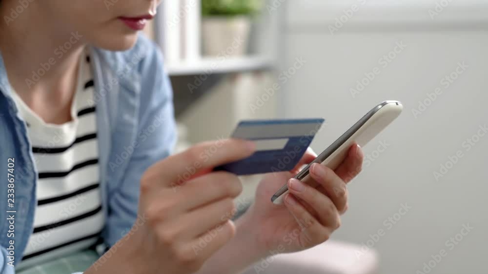 asian woman trying online payment for the package buying from summer sale. young lady sitting on the couch. focus video of girl holding credit card and confirm the number on smartphone. asian woman trying online payment for the package buying from summer sale. young lady sitting on the couch. focus video of girl holding credit card and confirm the number on smartphone.
