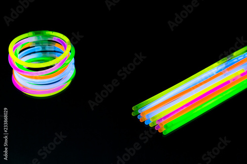 Colorful fluorescent light neon glow stick bracelet strap wristband on mirror reflection black background photo