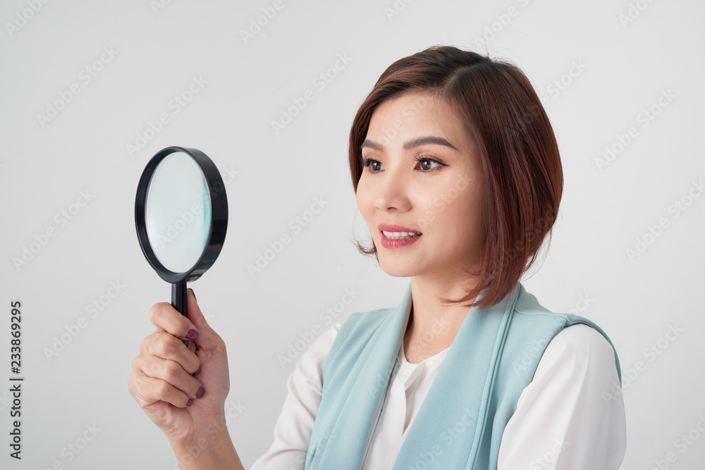 Close-up portrait of cheerful woman in blue suite looking at camera through magnifying glass, isolated over white background Close-up portrait of cheerful woman in blue suite looking at camera through magnifying glass, isolated over white background