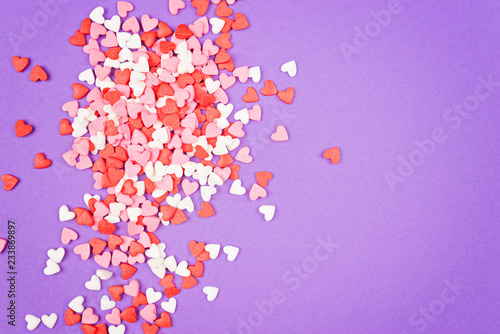 Many small multicolored sweet hearts are scattered on a violet background. Border. Flat lay. Copy space.