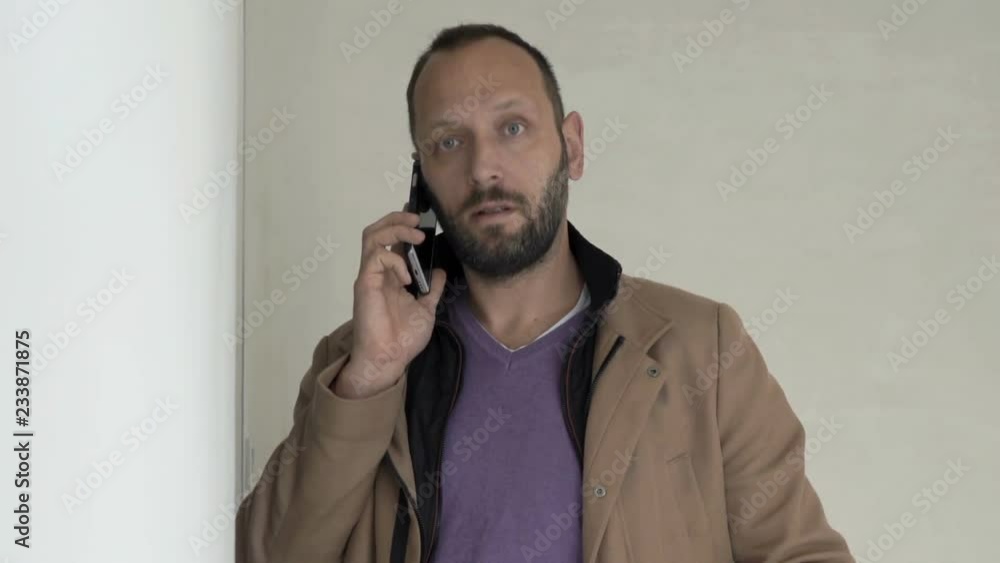 Young man talking on cellphone and checking wall at his new home Young man talking on cellphone and checking wall at his new home