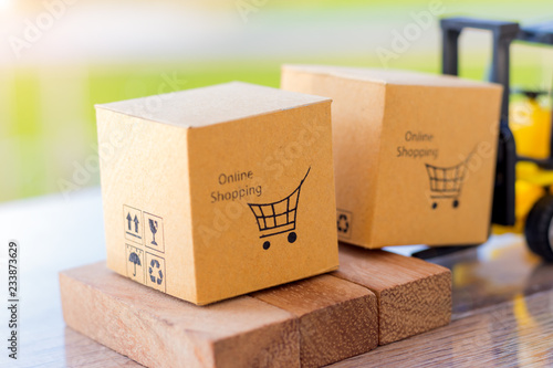Mini forklift truck load cardboard box with shopping cart symbol on wooden block with natural green background. Logistics and transportation management ideas and Industry business commercial concept.