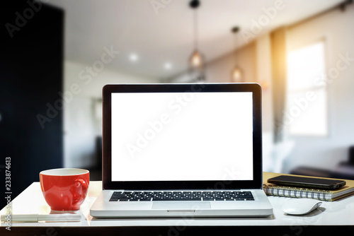 Front view of cup and laptop, smartphone, and tablet on table in office and background 