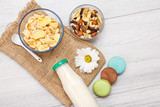 Glass bottle of milk, bowls with muesli and cornflakes on gray background