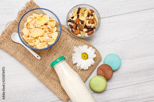 Glass bottle of milk, bowls with muesli and cornflakes on gray background
