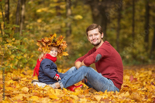 Father and daughter. They sit in the park and play with the leaves. Spending time together.