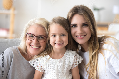 Happy family of grandmother, daughter and child girl looking at camera, smiling kid granddaughter posing with young mother and senior old mature grandma, three generations of women headshot portrait