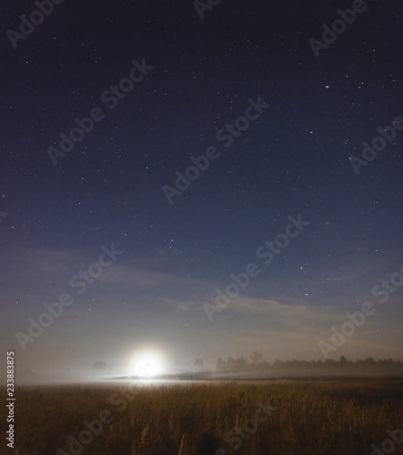 Moon setting in a misty field on a starry night