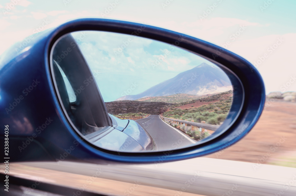 Driving blue car  through side mirror  with reflection of  beautiful Teide volcano  landscape in Tenerife, Canary island,Spain. Concept for travel and adventure.