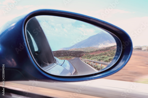 Driving blue car through side mirror with reflection of beautiful Teide volcano landscape in Tenerife, Canary island,Spain. Concept for travel and adventure.