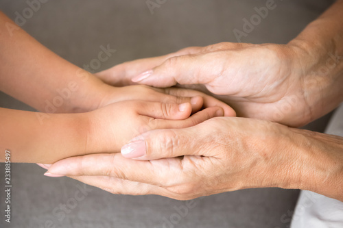 Close up view of senior grandmother holding hands of little kid granddaughter as concept of elderly granny protecting child, different old and baby generations, giving love care support to grandchild photo
