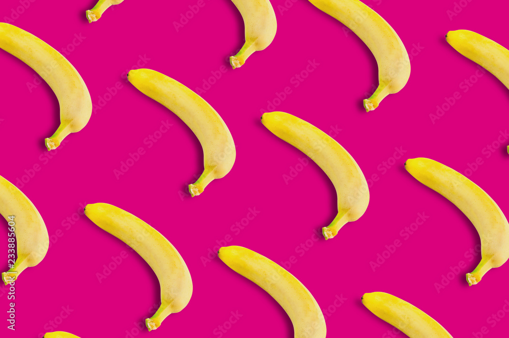 Diagonal rows of many fresh whole ripe bananas on pink background