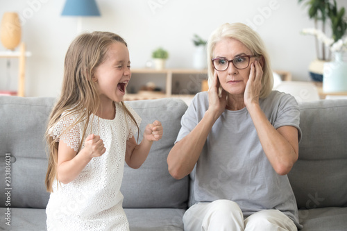 Bild auf Leinwand Shocked grandma closing ears not to hear noisy stubborn fussy little granddaught