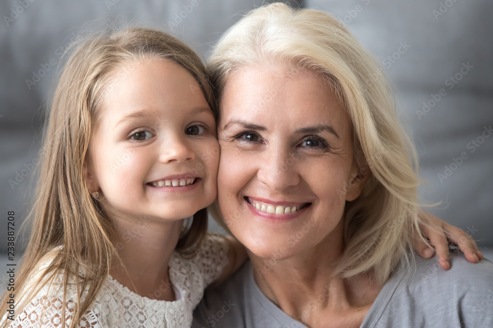 Happy old elderly grandmother hugging little smiling grandchild girl, loving senior grandma embracing cute kid granddaughter looking at camera, mature granny and child family headshot portrait Happy old elderly grandmother hugging little smiling grandchild girl, loving senior grandma embracing cute kid granddaughter looking at camera, mature granny and child family headshot portrait
