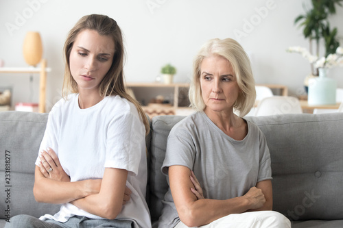 Upset older mother in law and adult daughter sit back to back not talking after fight disagreement, two stubborn old young women ignoring avoiding each other sad by argument, family conflict concept photo