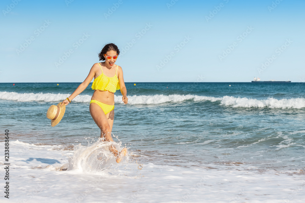 Happy smiling young woman in sun hat walking on beach along seaside, summer sea vacation and travel concept Happy smiling young woman in sun hat walking on beach along seaside, summer sea vacation and travel concept