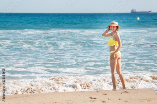 Happy smiling young woman in sun hat walking on beach along seaside, summer sea vacation and travel concept
