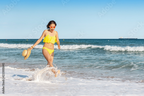 Happy smiling young woman in sun hat walking on beach along seaside  summer sea vacation and travel concept
