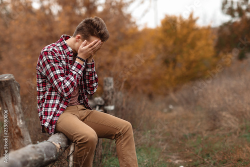 sad young man sitting on wooden fence