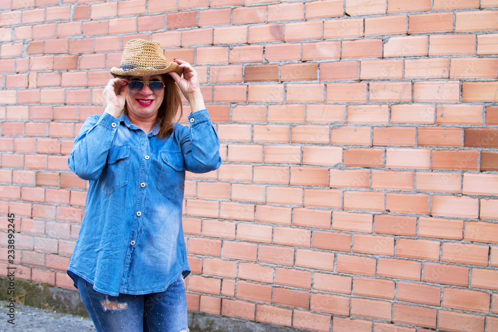 portrait of senior woman with sunglasses and straw hat in jeans