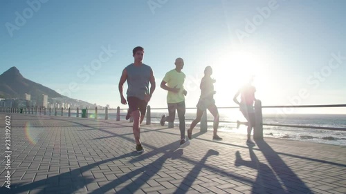 Group of young people running on ocean front. Runners in sportswear training together outdoors on a sunny day.
