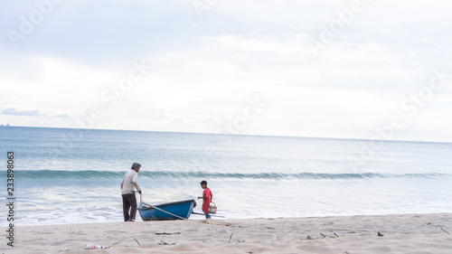 Grandfather and Grandson Pulling a Row Boat into the Sea to go Fishing