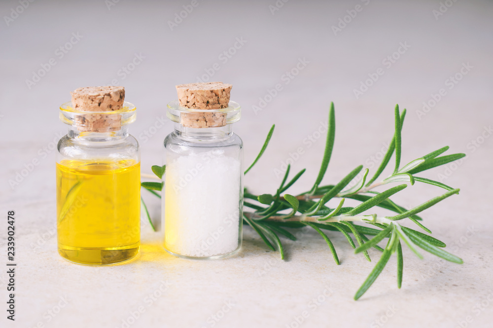 Rosemary essential oil in a small bottle and fresh twig on light background. Natural aroma cosmetic oil and salt Rosemary essential oil in a small bottle and fresh twig on light background. Natural aroma cosmetic oil and salt