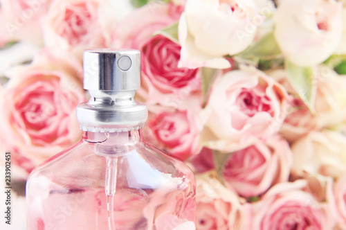 Spray perfume bottle closeup, pink rose blossom soft light background. 
